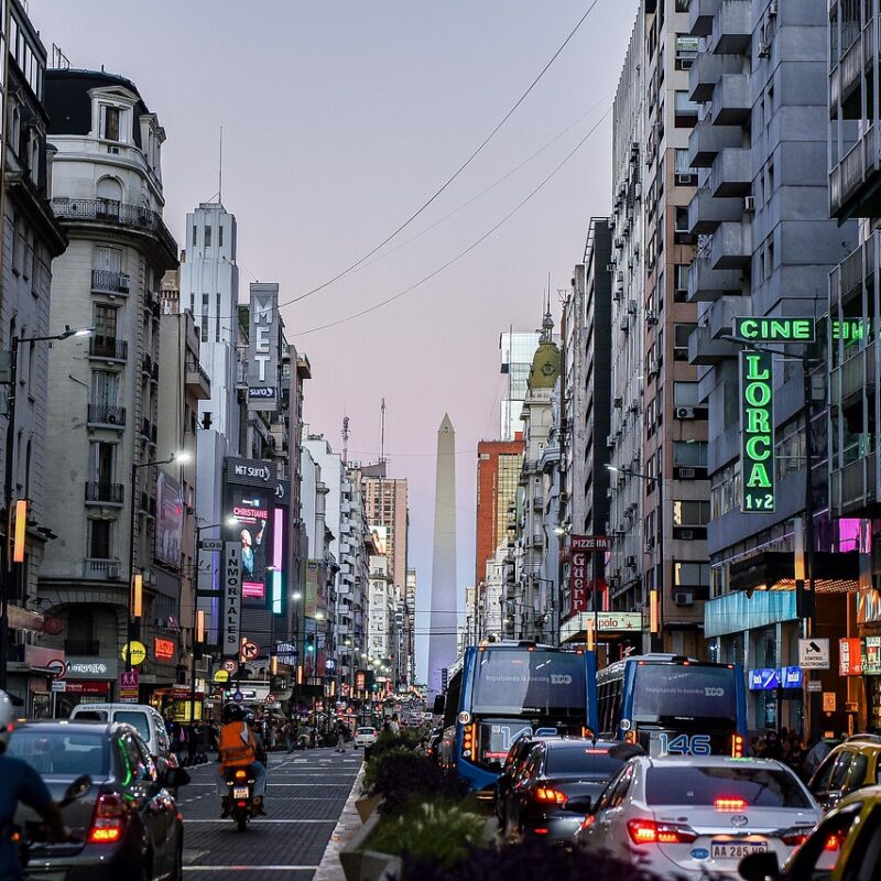 Neon-lit Buenos Aires street filled with queues of taxis, scooters, and dozens of cars
