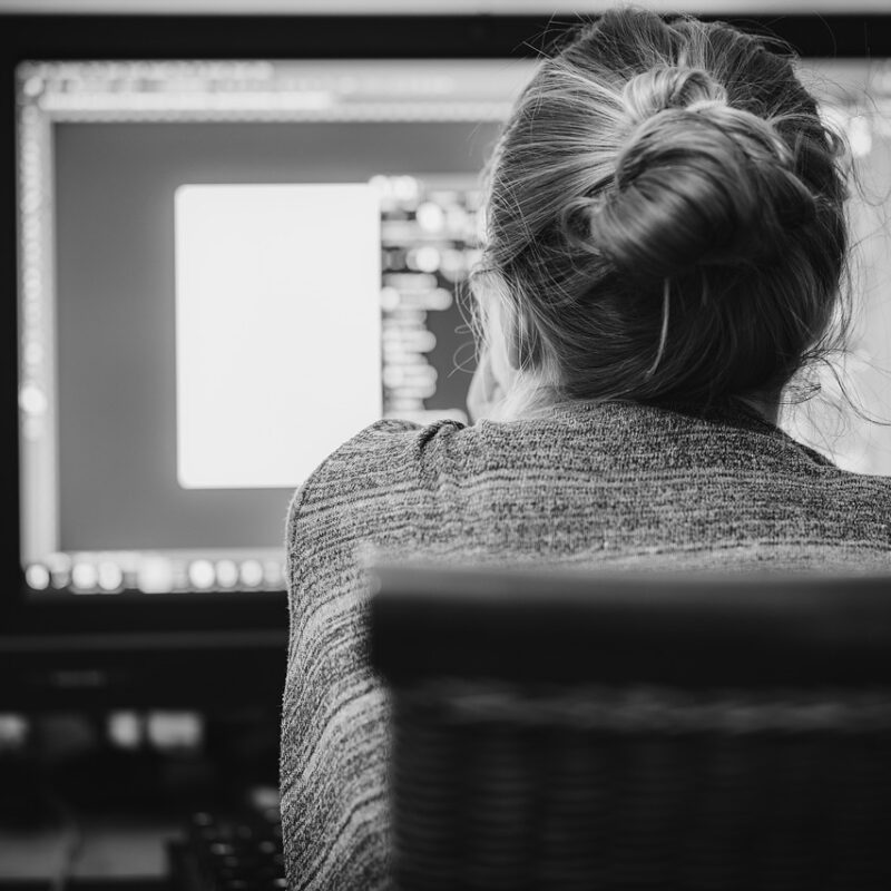 A black and white photograph of a woman working at a computer at home